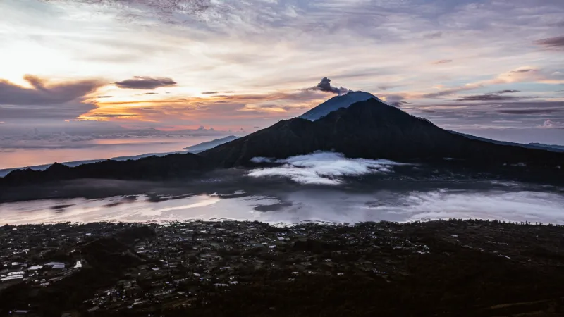 Mount Agung rising behind the Batur caldera at sunrise, cloud resting on the lake.