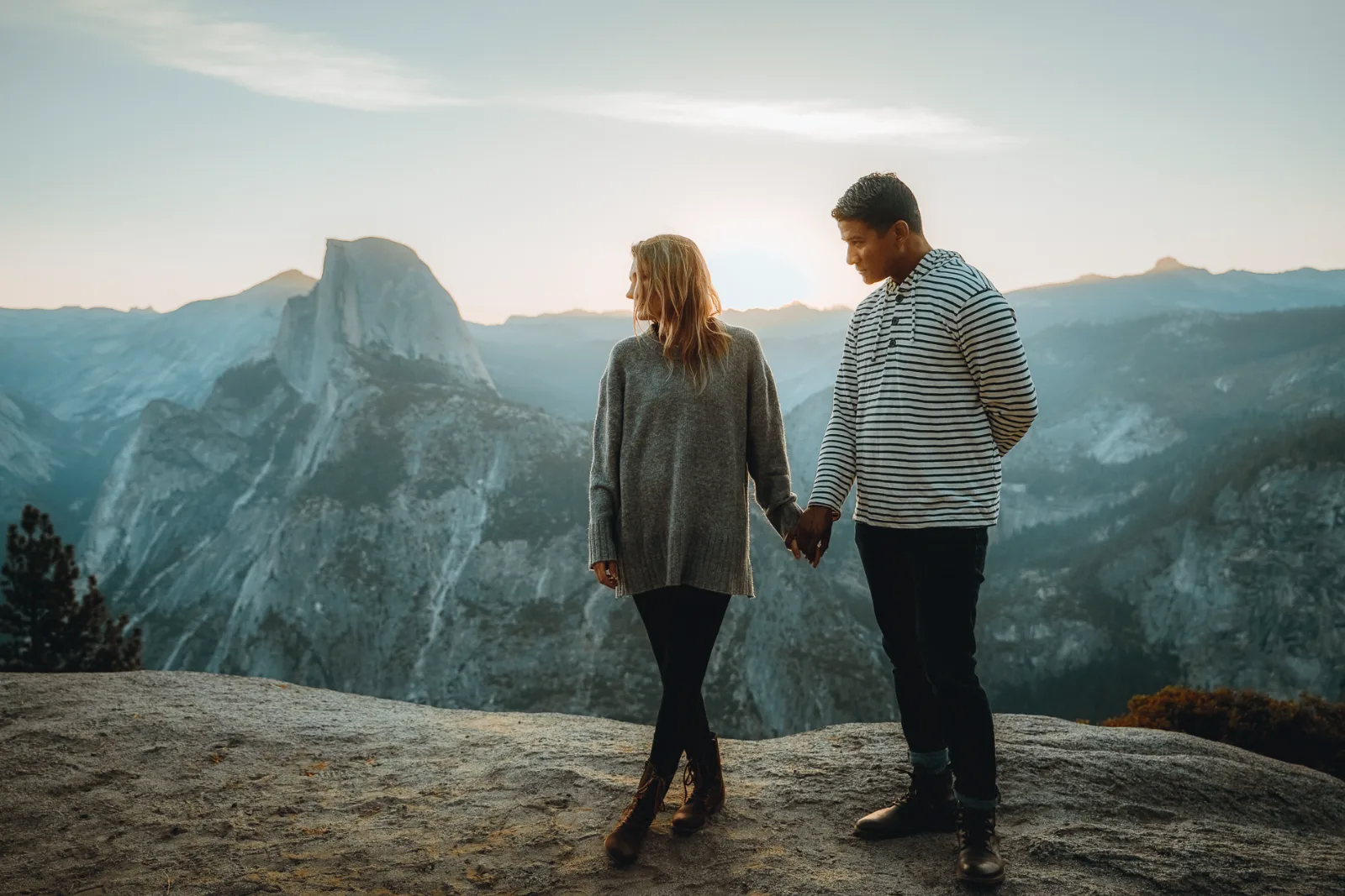 Two people holding hands on a granite overlook with a large granite dome behind them.